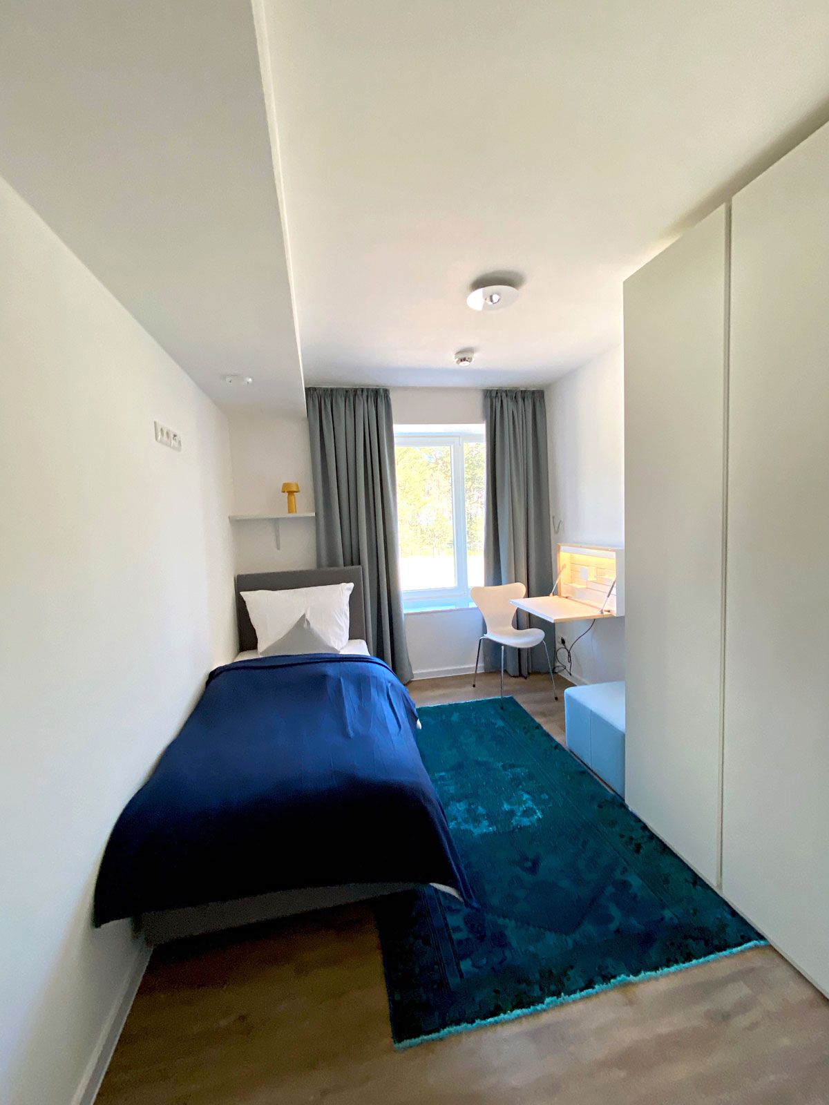 Ferienwohnungen in Prora - Vorhänge: Jab Anstoetz, Wand-Schreibtisch: Müller Möbelwerkstätten, Stuhl: Fritz Hansen, Kleiderschrank: Cramer Holzmanufaktur, Hocker: Signet, Boxspringbett: FBF Hotelbetten, Wandboard: Cramer Holzmanufaktur, LED-Nachttischleuchte: Marset, Teppich: Vintage Unique