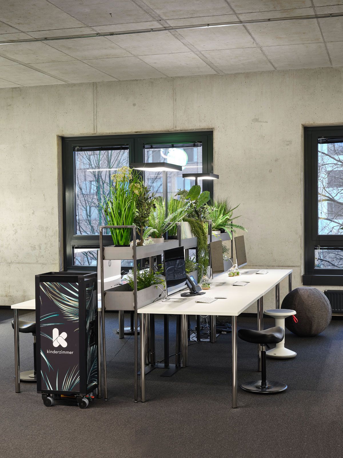 Headquarter einer Kita - Trolley von Bordbar, Tische und Raumteiler aus der Cramer Holzmanufaktur, Sattelhocker Move von Varier, kleiner weißer Hocker von Interstuhl, Leuchten von Molto Luce