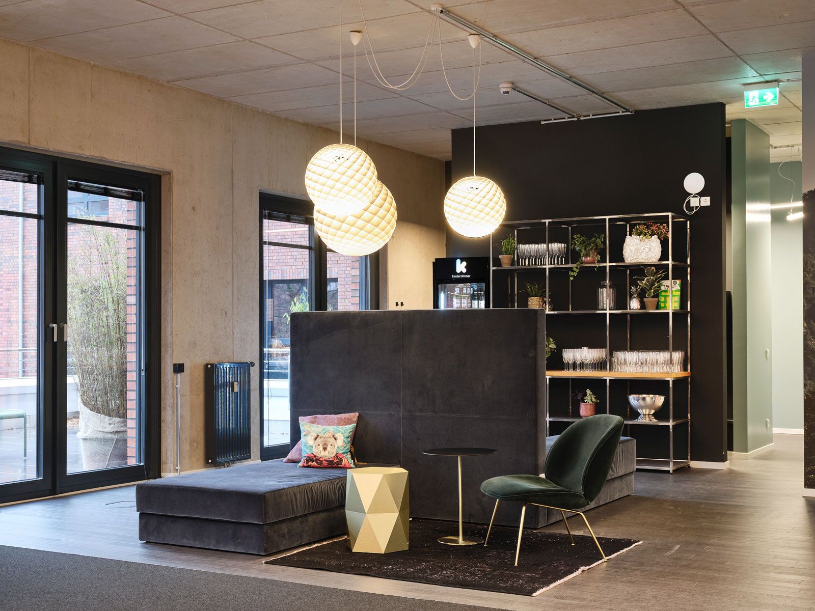 Headquarter einer Kita - Lounge-Sitzbank aus der Cramer Polstermanufaktur, Sessel von Gubi, Pendelleuchten Patera von Louis Poulsen, goldener Beistelltisch von FORMvorRAT, Schlosser-Regale von Cramer, Teppich Vintage