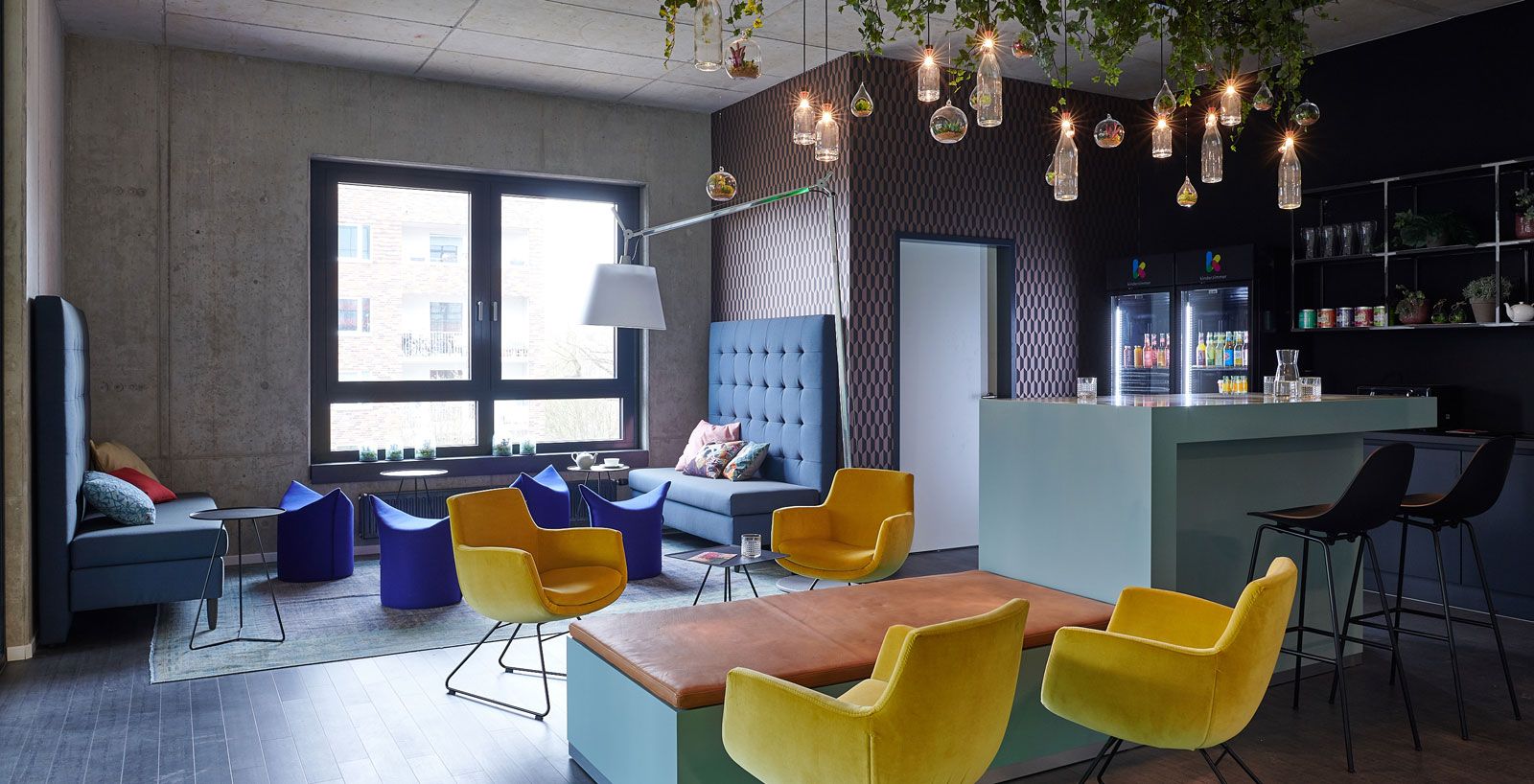 Headquarter einer Kita - Lounge-Bereich: Stühle Pia aus der Cramer Polstermanufaktur, Bänke von Signet, Beistelltische von Möller Design, Stehleuchte Tolomeo Mega von Artemide, Hocker Zipfel von Werther, Tresen aus der Cramer Holzmanufaktur, Flaschenleuchten von Wever und Ducre, Barhocker Vintage